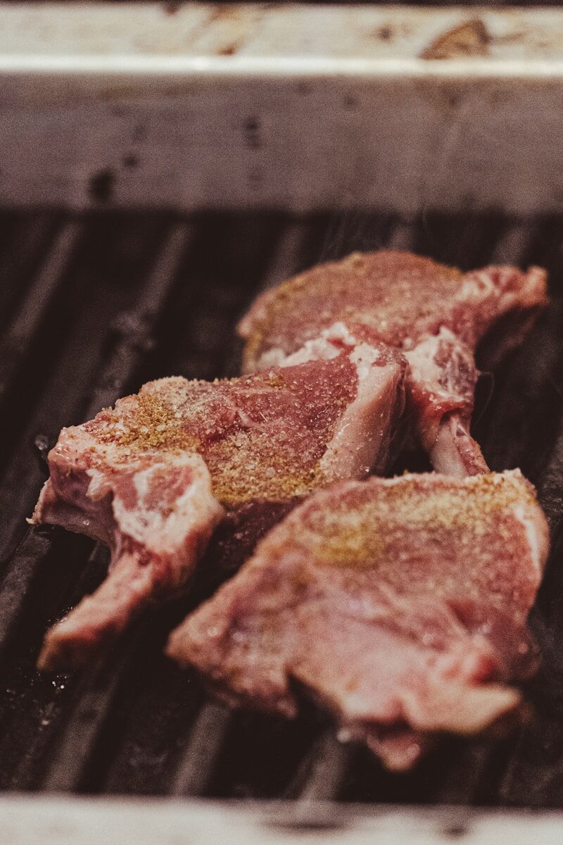 Three seasoned meat chops cooking on a hot grill.